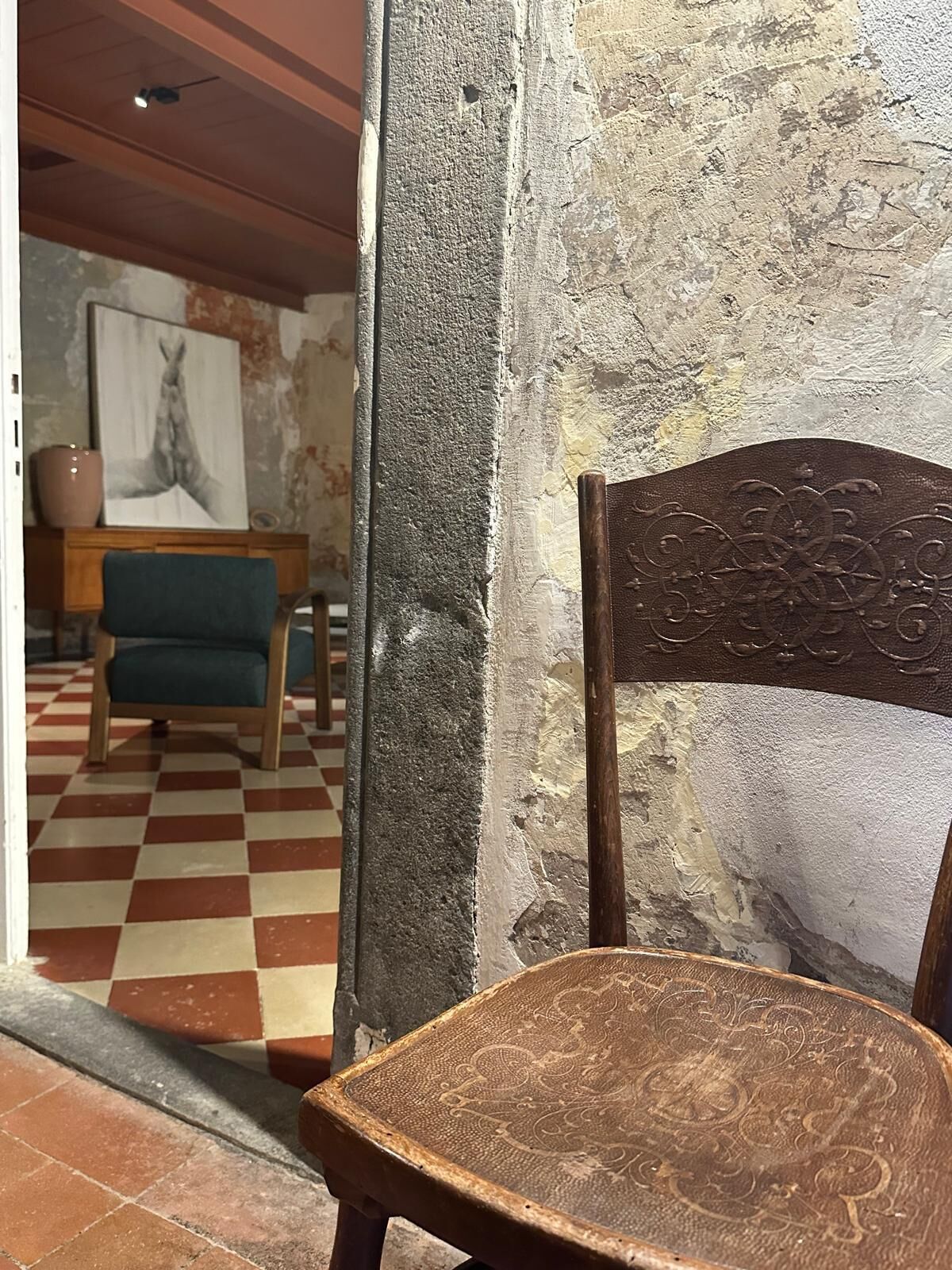 A rustic interior with a wooden chair, a checkered floor, and a painting on the wall.