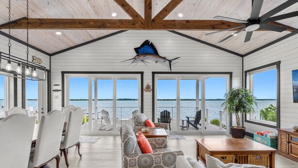 Un vaste espace de vie doté d’une grande fenêtre donnant sur la mer, d’un ventilateur de plafond et d’un coin repas avec des chaises et une table.