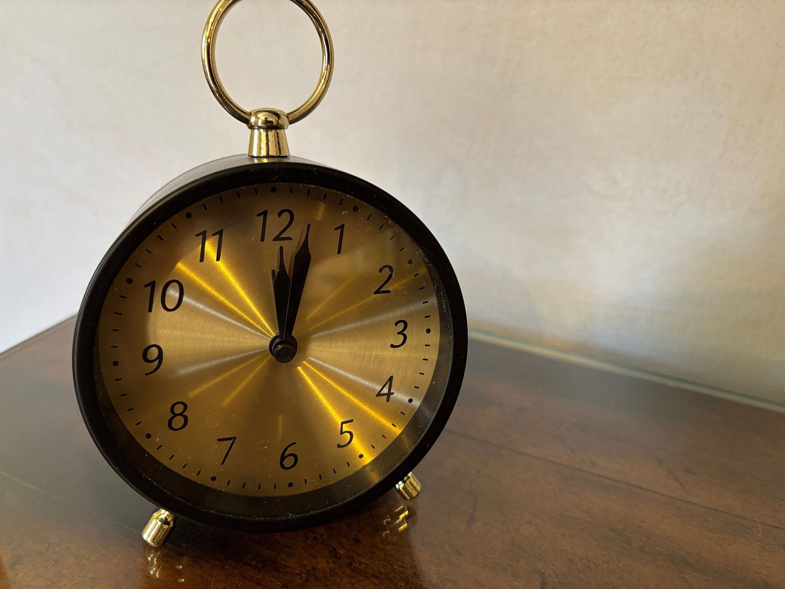 A vintage wall clock with a gold face and black hands, mounted on a wooden surface.