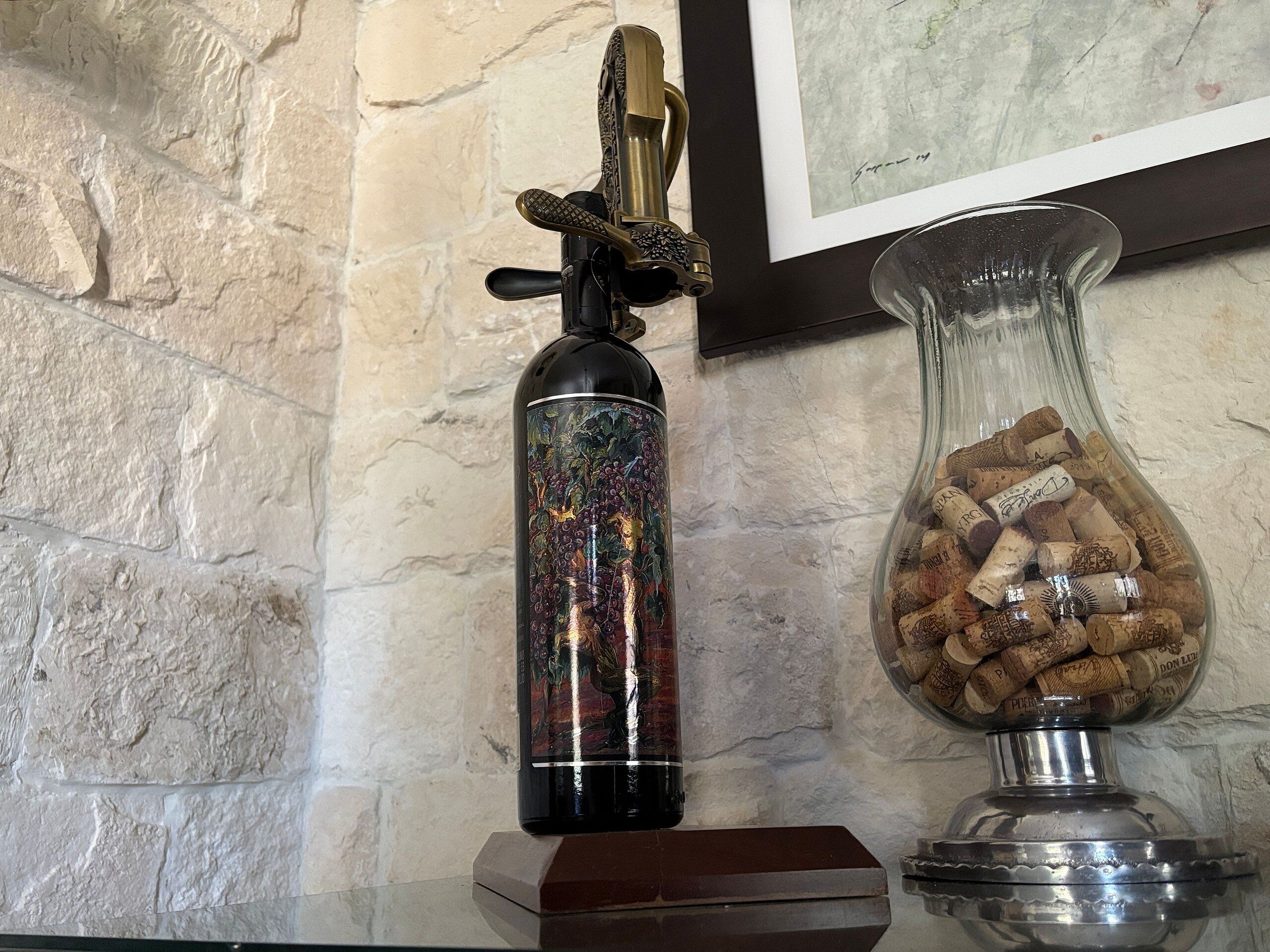 A decorative bottle with a metallic cap, a glass vase with corks, and a framed artwork on a textured wall.