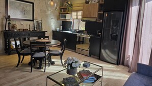 A modern kitchen with a black refrigerator, a microwave, and a gas stove. There is a dining area with a round table and chairs, and a glass coffee table with books and flowers. - Loft Carrara (Val'Quirico)