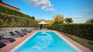 Une piscine rectangulaire avec une terrasse carrelée, entourée de haies soigneusement taillées et d’un mur en pierre.