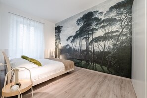 Un dormitorio con cama, mesita de noche, lámpara y un mural grande con motivos forestales en la pared.