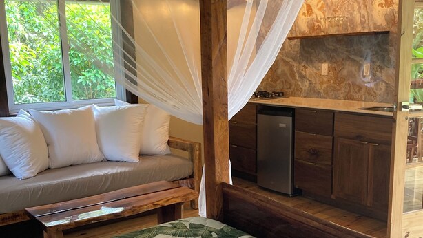 Une chambre à coucher comprenant un lit, un canapé, un banc, un téléviseur et une fenêtre donnant sur un paysage verdoyant.
