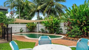 Un jardin avec une piscine, une table blanche et des chaises.