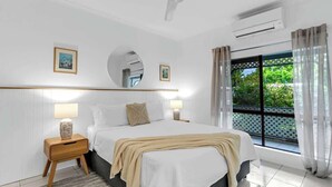 Une chambre d’hôtel avec un lit, des lampes de chevet, un miroir rond, une fenêtre avec des rideaux et une vue sur la verdure.