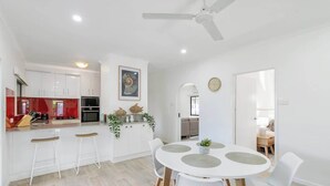 Une cuisine moderne avec des meubles blancs, un coin repas doté d’une table ronde et de chaises, et un ventilateur de plafond.