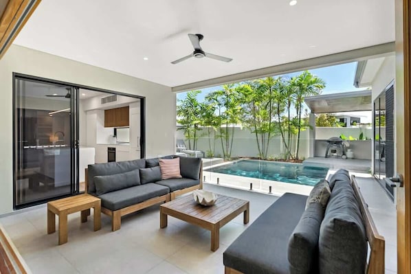 A modern living room with a sofa, coffee table, and a pool area visible through glass doors.
