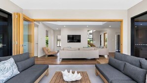 A modern living room with a sofa set, a coffee table, and a TV mounted on the wall. - Sea Mist—Poolside Oasis near Palm Cove Beachfront (Palm Cove)