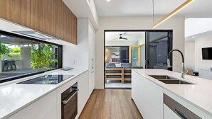 A modern kitchen with white cabinetry, a built-in oven, and a large window. - Sea Mist—Poolside Oasis near Palm Cove Beachfront (Palm Cove)