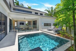 A modern house with a swimming pool, glass doors leading to a living area, and outdoor seating.