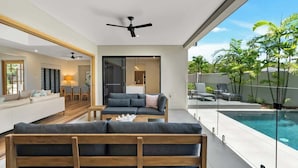 A modern living room with a sofa, coffee table, and a view of a swimming pool. - Sea Mist—Poolside Oasis near Palm Cove Beachfront (Palm Cove)