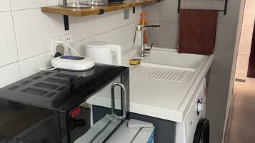 Una cucina compatta con microonde, frigorifero e lavandino. Ripiani sopra il bancone contengono diversi oggetti.