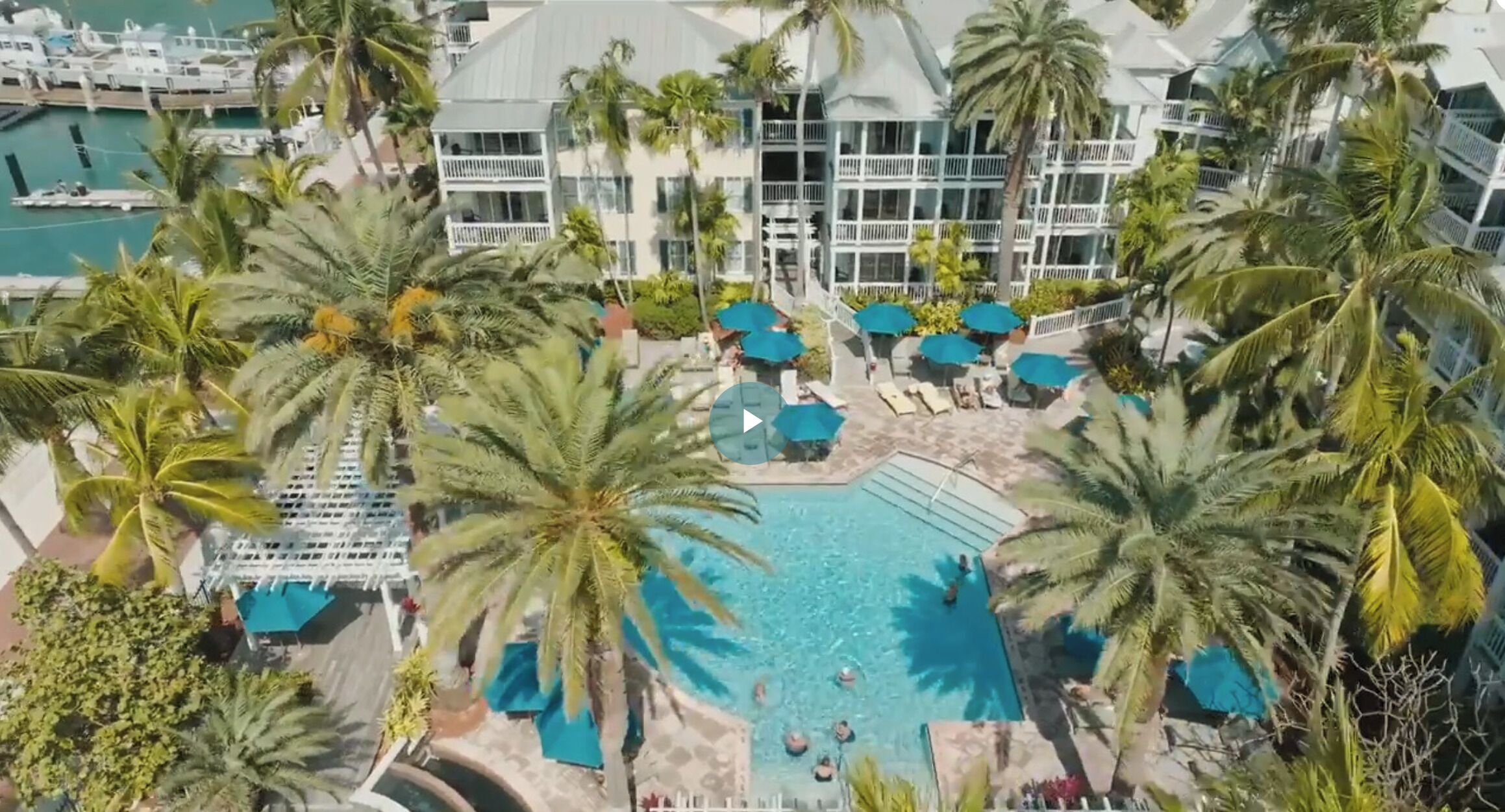 A resort with a central pool surrounded by palm trees and lounge chairs.