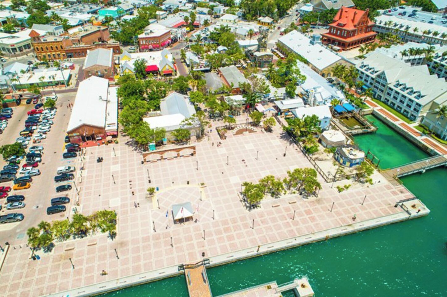 An aerial view of a coastal area with a large parking lot, a central plaza, and buildings with varied architecture.