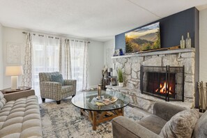 A living room with a fireplace, a sofa, a chair, and a glass coffee table.