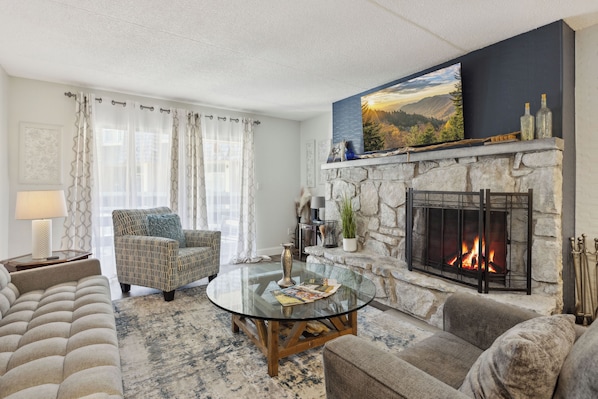 A living room with a fireplace, a sofa, a chair, and a glass coffee table.