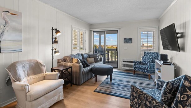 A living room with a sofa, armchair, and ottoman, a television, and a balcony with a view. - A Place At The Beach IV #228 (Myrtle Beach)