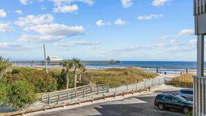 A coastal view with a pier extending into the ocean, a parking area, and a building with a green roof. - A Place At The Beach IV #228 (Myrtle Beach)