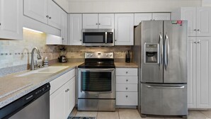 A modern kitchen with white cabinets, stainless steel appliances including a microwave, oven, and refrigerator, and a dishwasher. - A Place At The Beach IV #228 (Myrtle Beach)