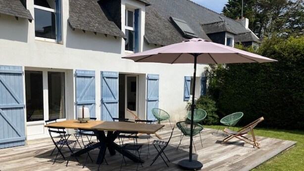 An outdoor patio with a wooden table and chairs, a large umbrella, and a glass chair. - House CARNAC - 300 meters from Légenèse beach (Carnac)