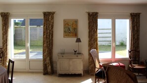 A room with a large sliding glass door leading to a garden, a white cabinet with a lamp, and two wicker chairs. - House CARNAC - 300 meters from Légenèse beach (Carnac)