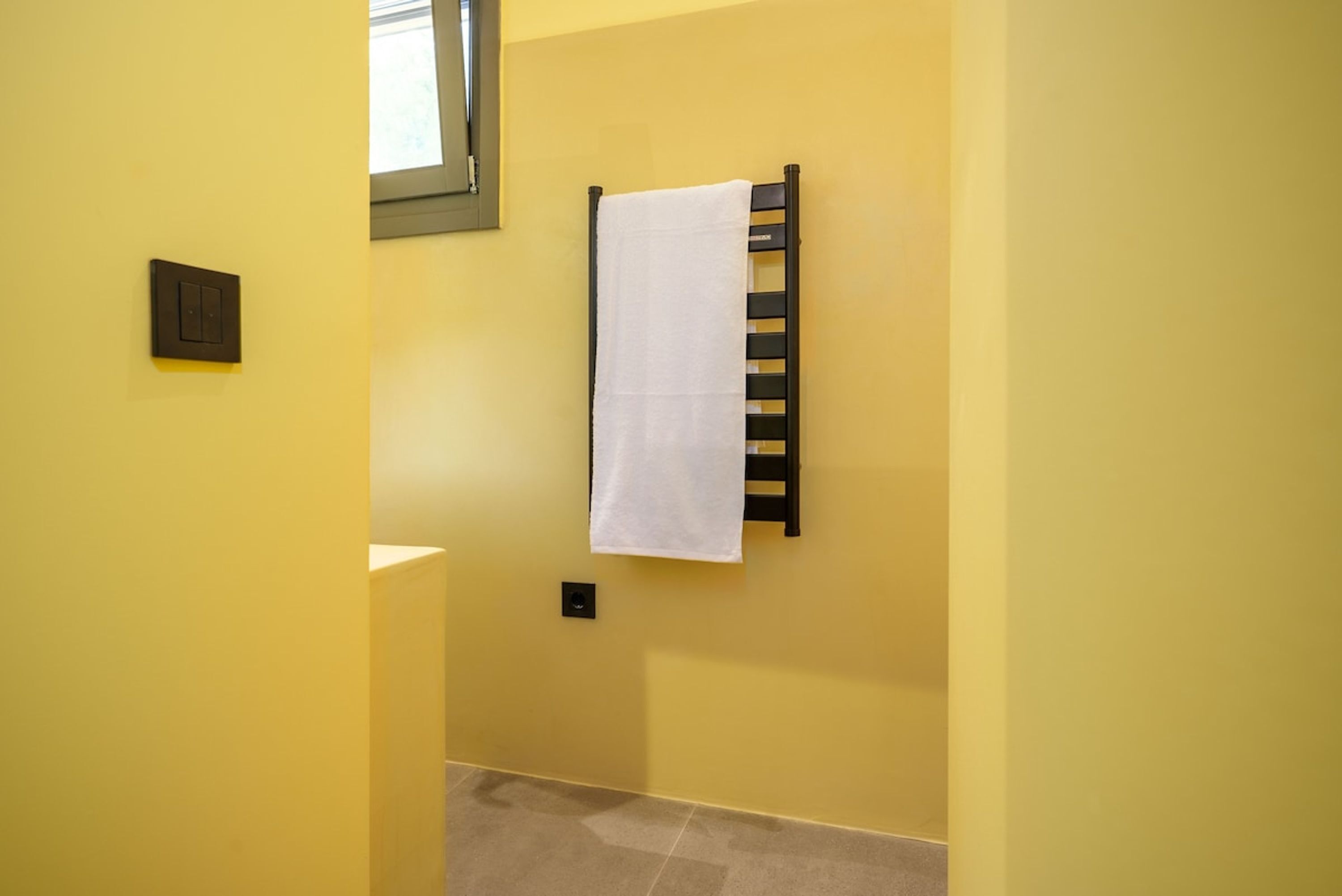 Ein Badezimmer mit gelben Wänden, ein weißes Handtuch an einem Handtuchhalter und ein Fenster über dem Handtuchhalter.