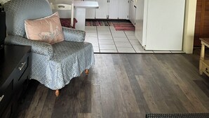 A compact kitchen with a microwave, sink, and refrigerator. There is a chair with a cushion and a ceiling fan.