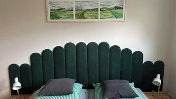 Ein Schlafzimmer mit kariertem Bettbezug, zwei Kissen, einem Kopfteil und einem gerahmten Landschaftsbild über dem Bett.