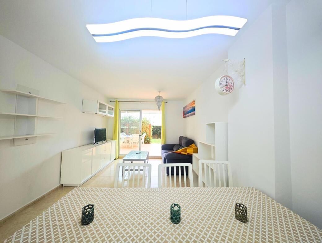 A bright living room with a sofa, a TV, and a dining table with chairs.