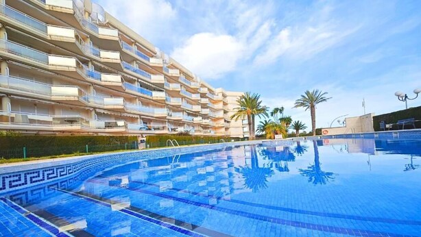 Una piscina con un diseño geométrico de azulejos, rodeada por un edificio de varios pisos con balcones.