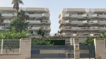 Un edificio residencial de varios pisos con balcones, una entrada con reja y una palmera en primer plano.