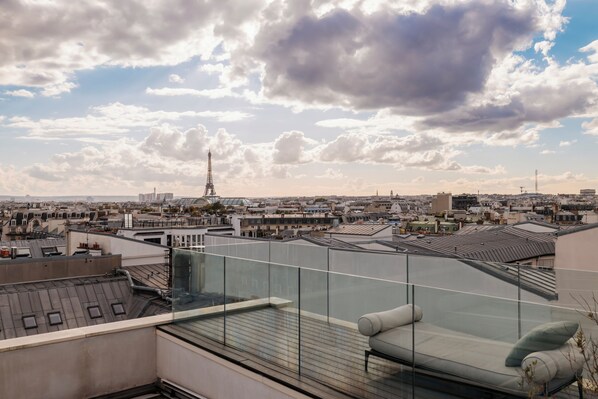 A rooftop terrace with a glass balustrade, a cushioned seating area, and a view of the Eiffel Tower in the distance. - Hôtel de Pourtalès (Paris)