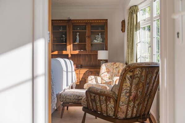 Une pièce avec un meuble en bois, un fauteuil à motifs et un lit recouvert d’une couverture à rayures.