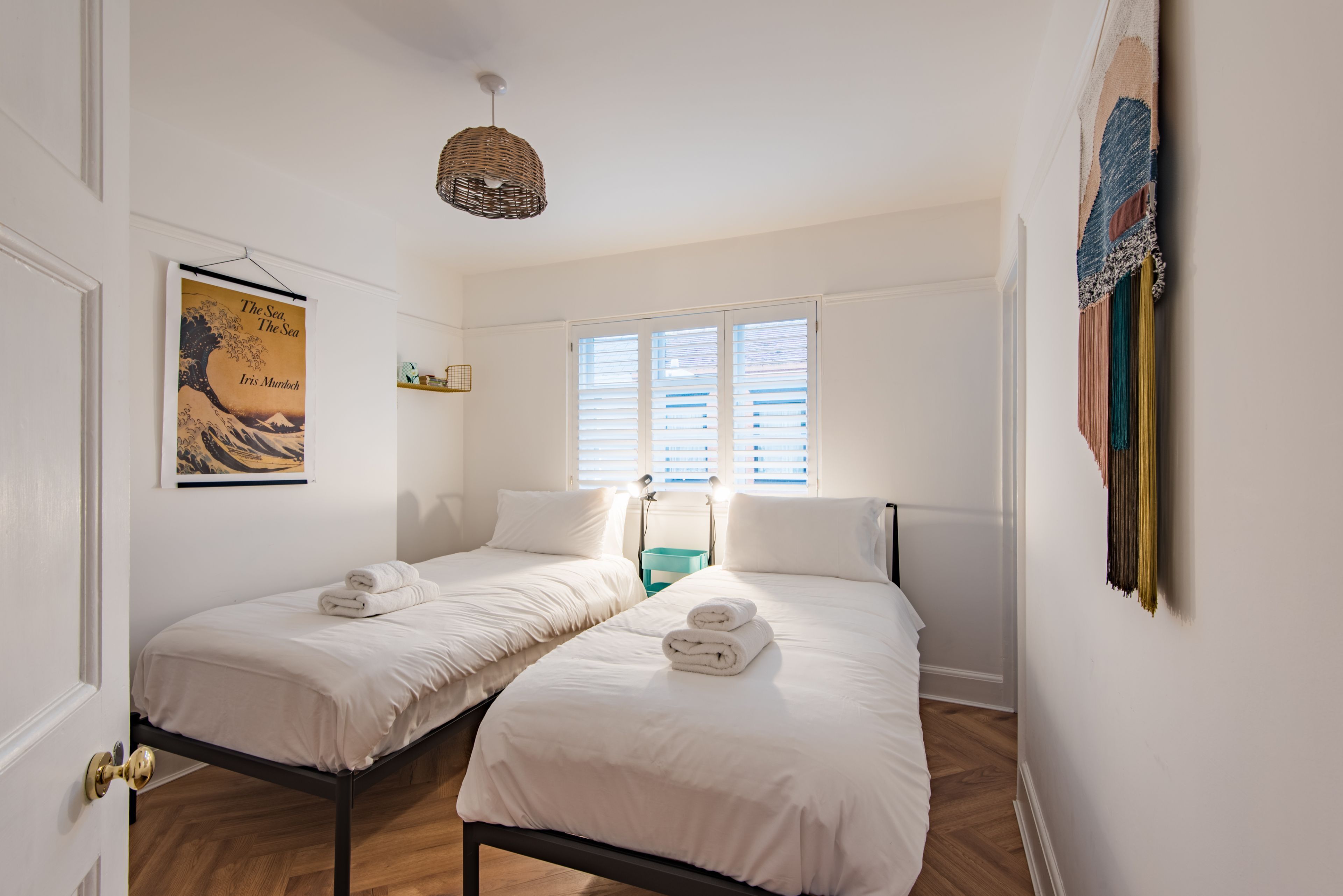 Een hotelkamer met twee eenpersoonsbedden, een groot raam met zonwering, een hanglamp en een wanddecoratie.