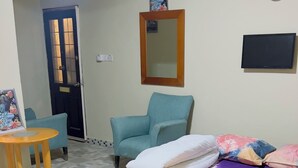 Una stanza con un letto, due poltrone, un tavolino, uno specchio e una sveglia appesa al muro.
