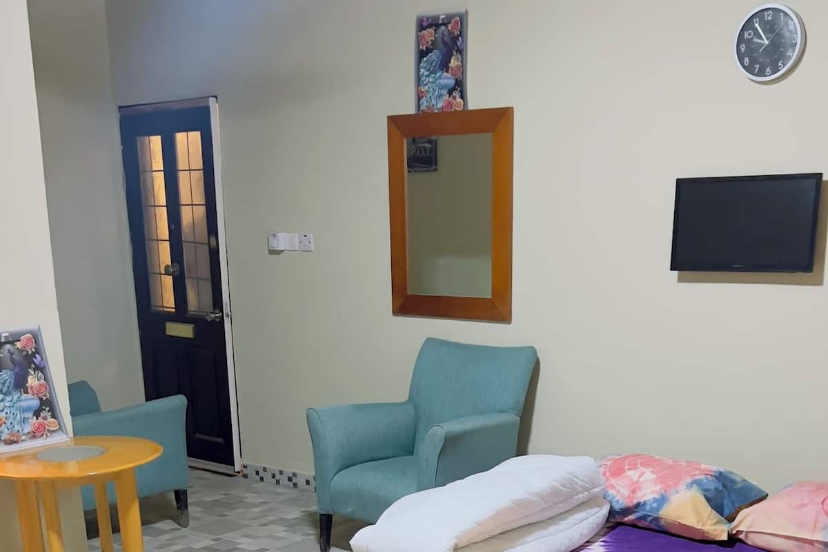 Quarto com cama, duas poltronas, uma mesinha, espelho e relógio na parede.