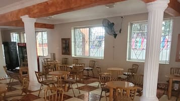 A spacious room with checkered flooring, wooden tables and chairs, and large windows.