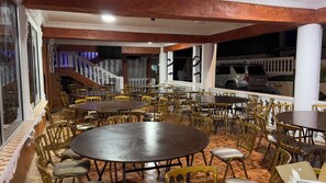 A restaurant with multiple round tables and chairs, a staircase, and a view of parked cars outside. - Brownerts Resort (Freetown)