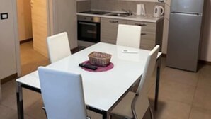 A compact kitchen with a dining table, chairs, and basic appliances. - 04. Apartment (Signa)