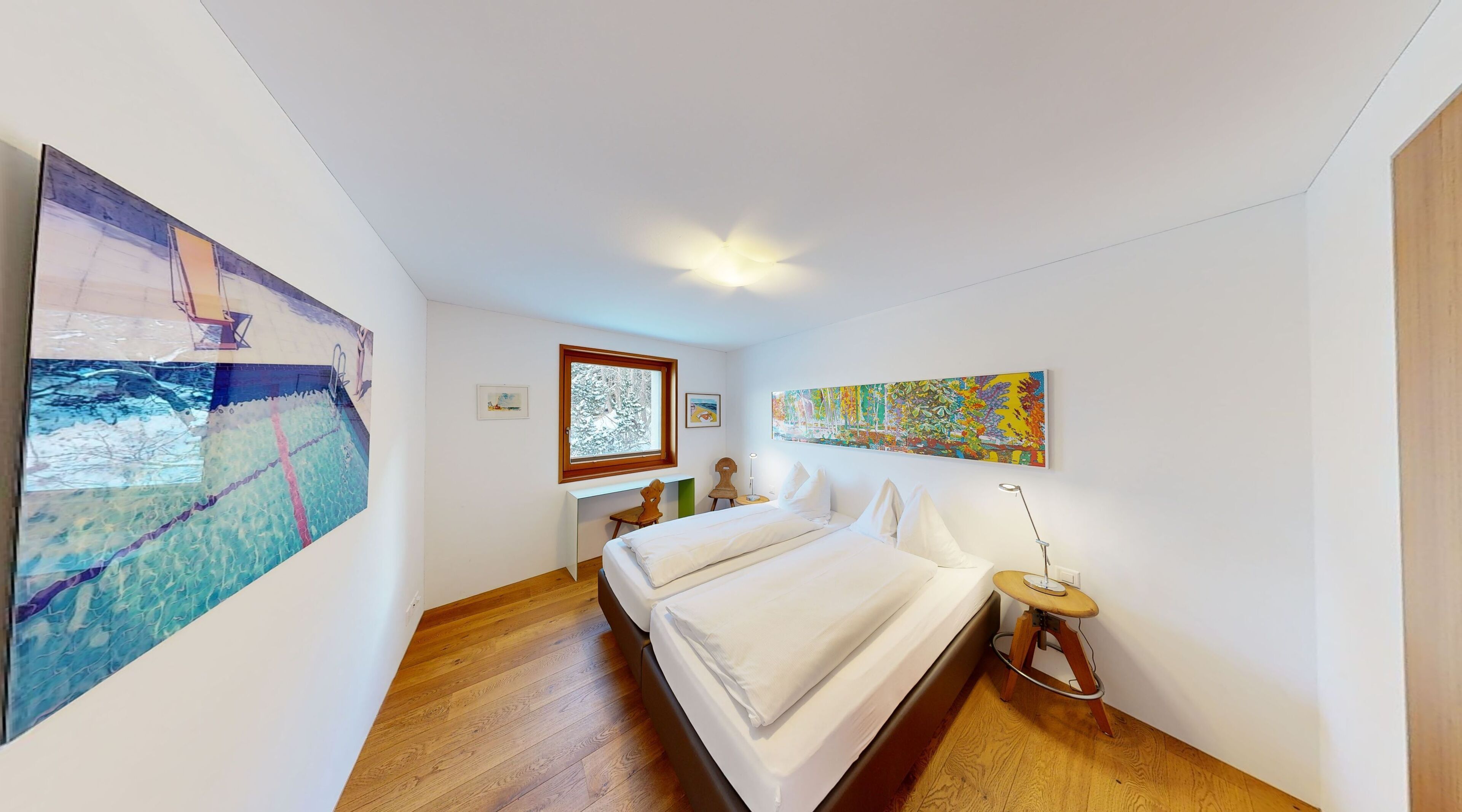 A bedroom with two beds, wooden flooring, and artwork on the walls.