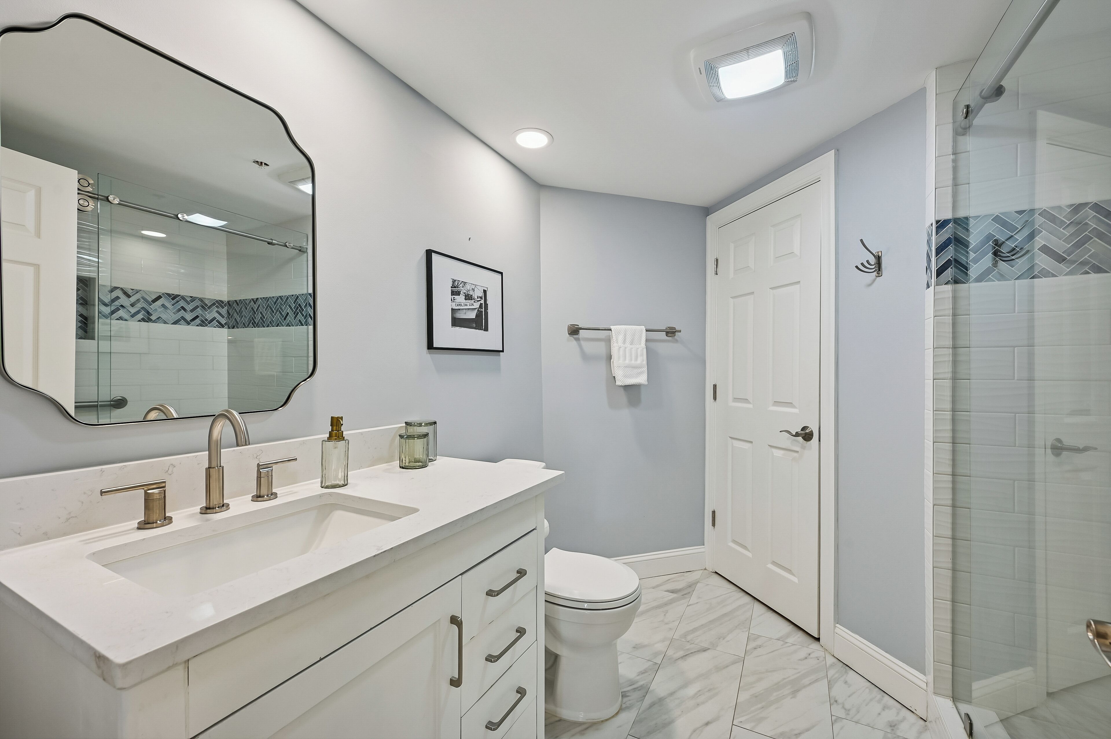 A modern bathroom with a large mirror, a white sink, a toilet, and a shower area.
