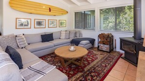 A cozy living room with a sofa, a coffee table, a fireplace, and a surfboard on the wall.