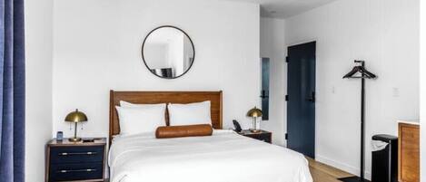 A neatly arranged bedroom with a wooden bed, two bedside tables with lamps, a round mirror on the wall, and a black floor lamp.
