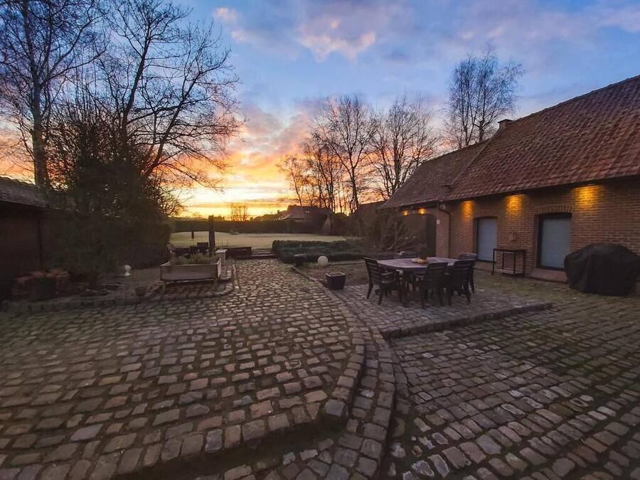 A courtyard with cobblestone paving, a round table with chairs, and a brick building with a tiled roof.