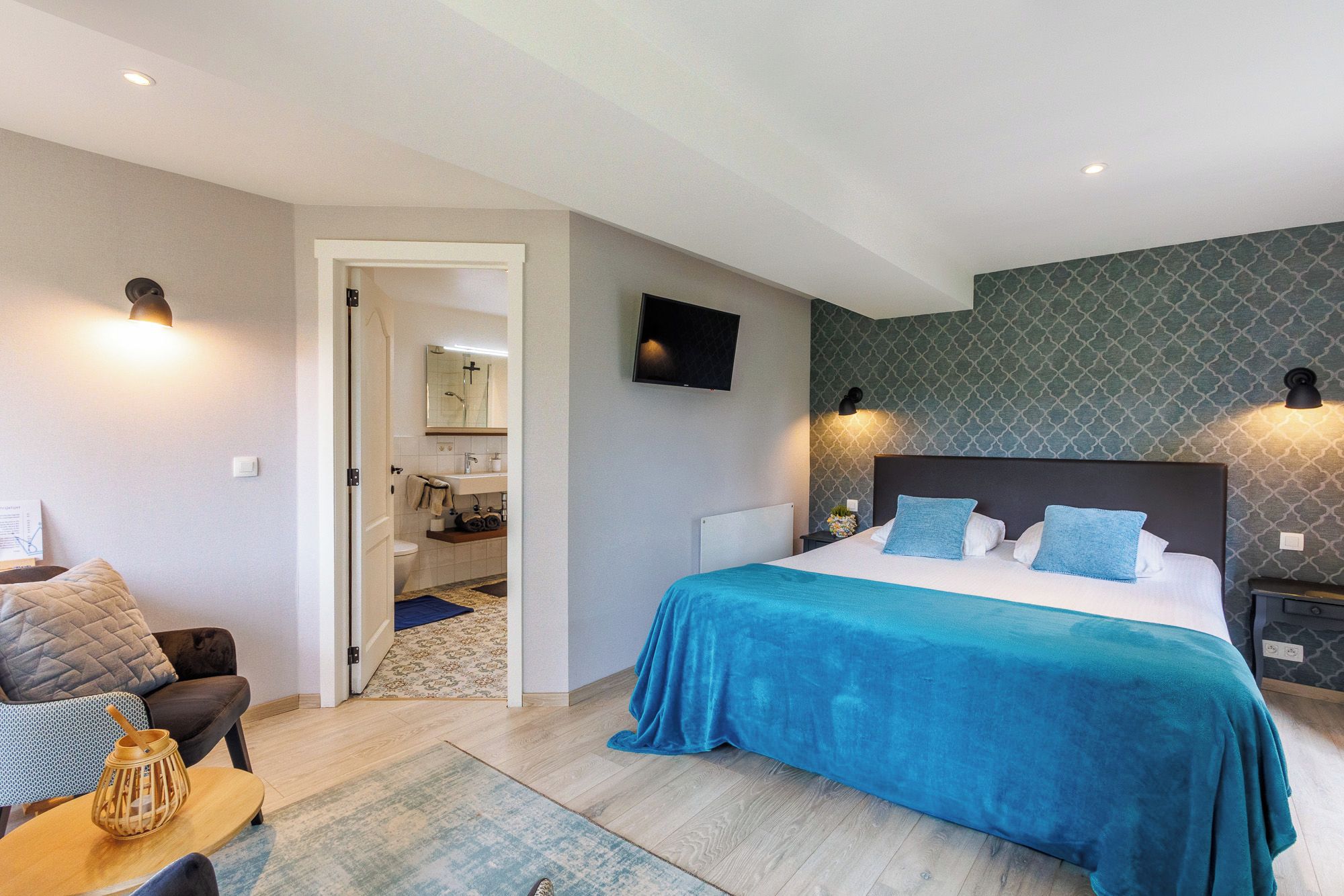 Une chambre moderne avec un grand lit, une télévision et une salle de bain visible à travers une porte ouverte.