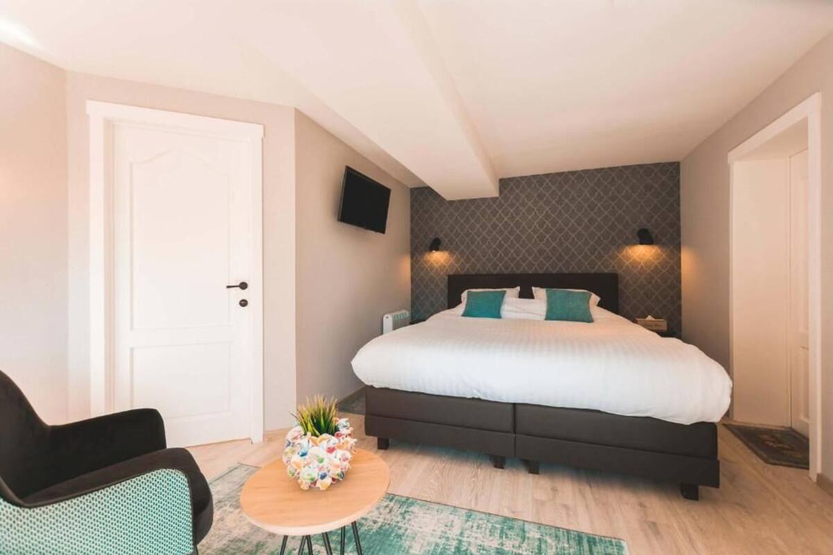 Ein Schlafzimmer mit einem großen Bett, einem kleinen runden Tisch mit einer Pflanze, einem schwarzen Stuhl und einem an der Wand befestigten Fernseher.