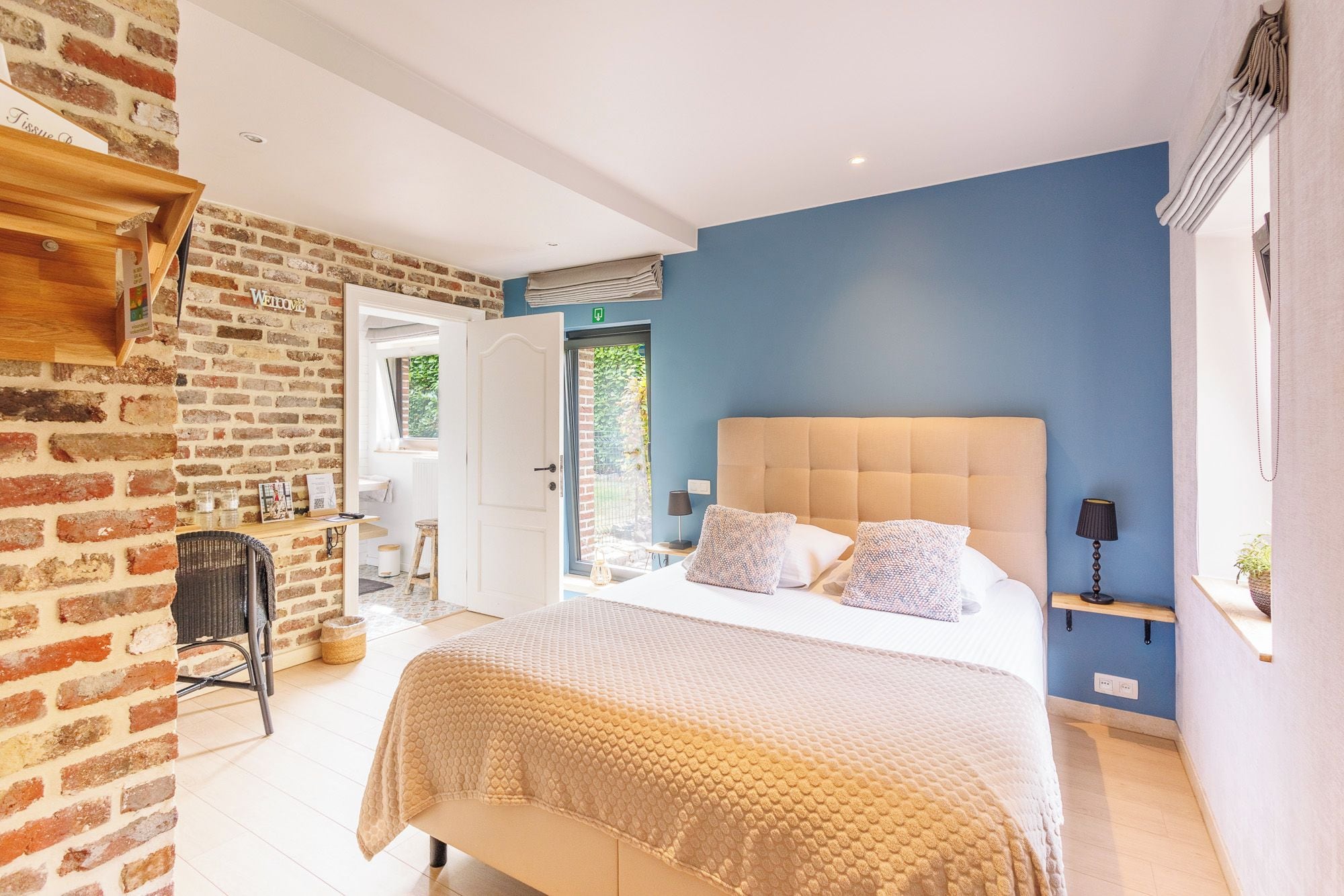 A bedroom with a brick wall, a bed with a beige headboard, and a blue accent wall.