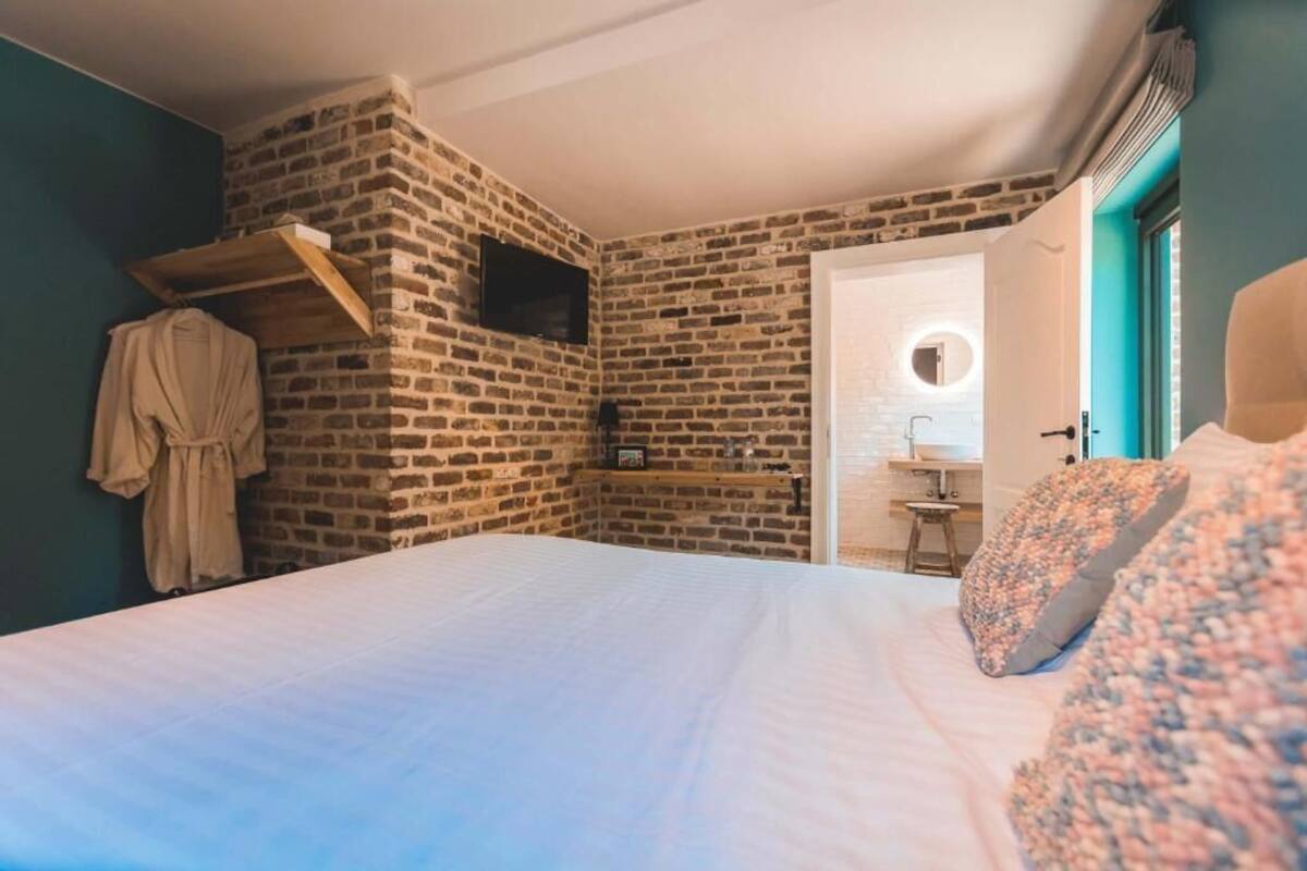 Ein Schlafzimmer mit Backsteinwand, einem Bett mit weißer Bettwäsche, einem aufgehängten Bademantel und einem an der Wand montierten Fernseher.