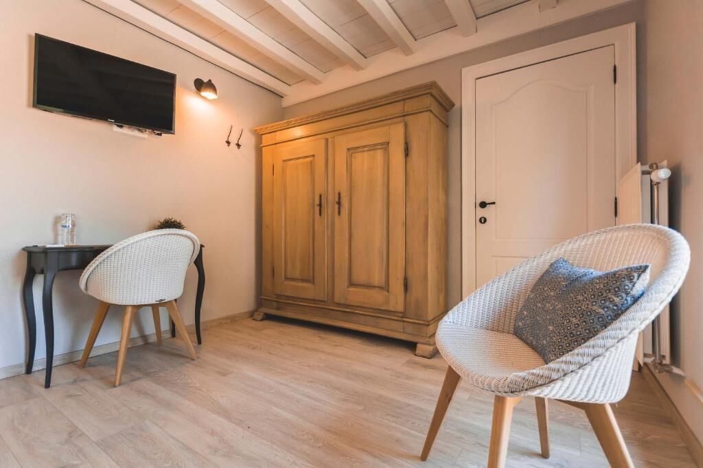 Una habitación con un armario de madera, un televisor montado en la pared, una silla de mimbre con cojín y una mesita con un vaso.